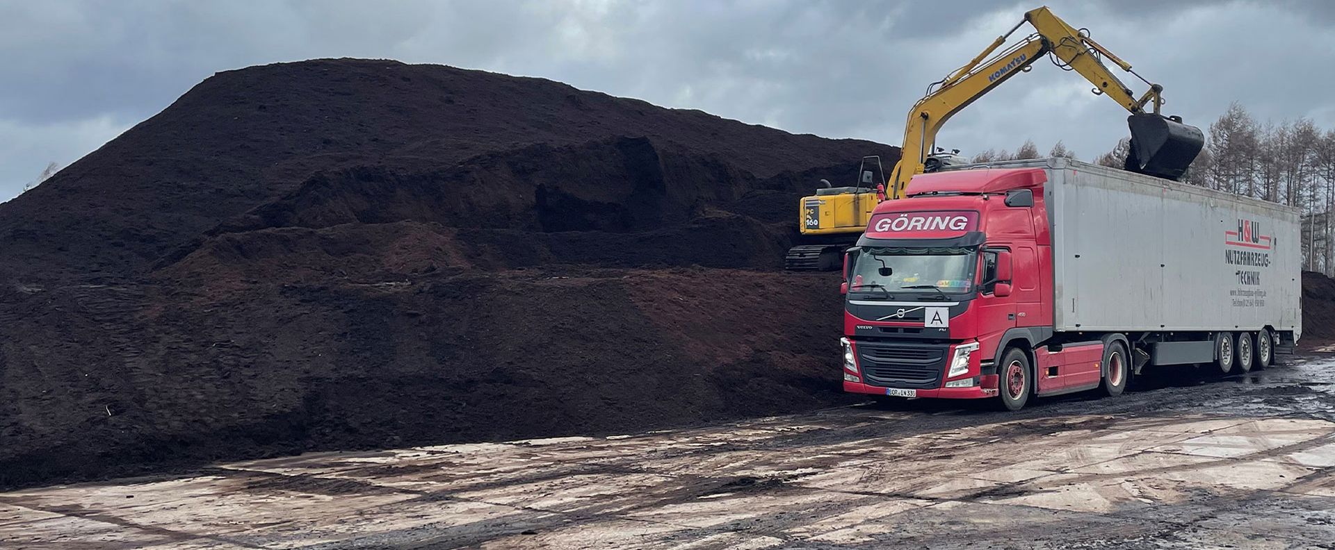 Ein roter Lkw mit einem Bagger, der Erde auf einen großen Erdhaufen lädt.